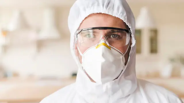 Mold remediation technician in a respirator, protective hood and safety glasses