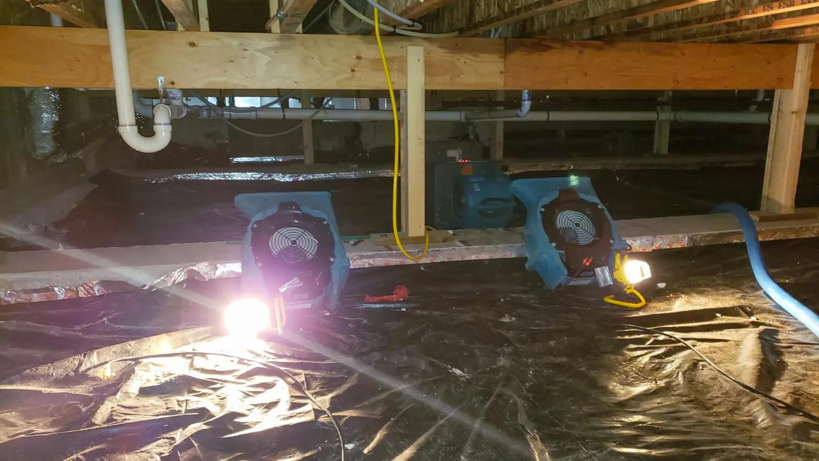 Crawl space with a vapor barrier, drying fans and lighting under floor framing