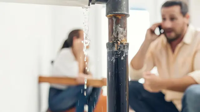 Homeowner on the phone while water drips from a pipe in the room