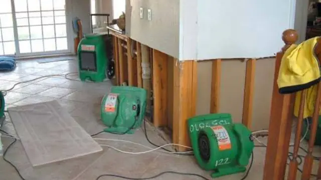 Drywall cut away at the base of a wall with dehumidifiers drying the cavity